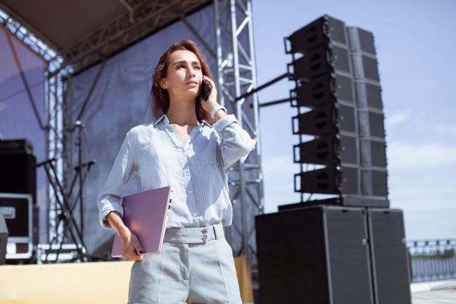 A music manager is standing in front of a stage talking on a cell phone.