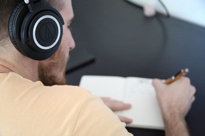 A man wearing headphones is writing in a notebook.