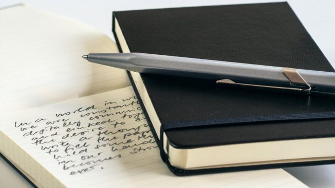 A pen rests on top of a black notebook