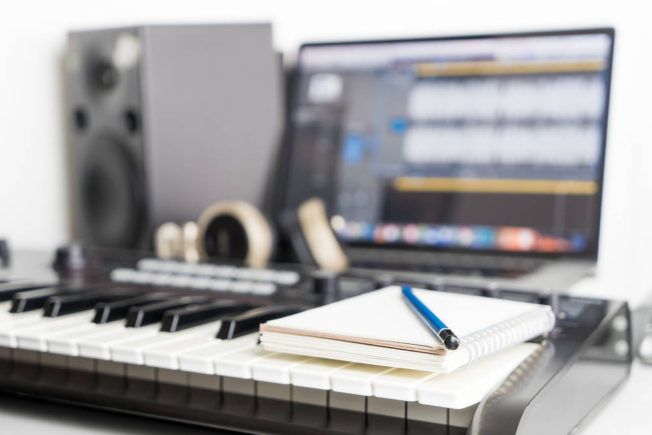 A keyboard with a notebook and pen on it next to a laptop.