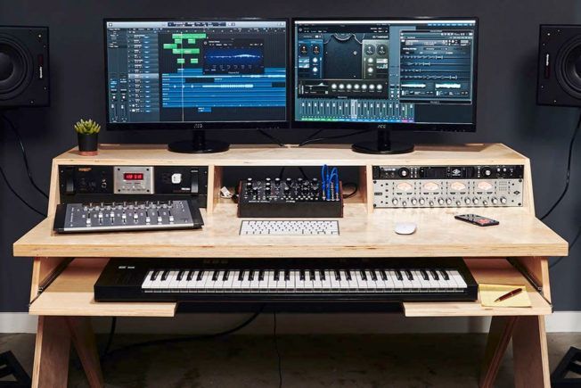 A recording studio with two monitors , a keyboard , and a piano.