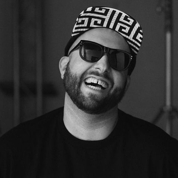 A man wearing a hat and sunglasses is smiling in a black and white photo.