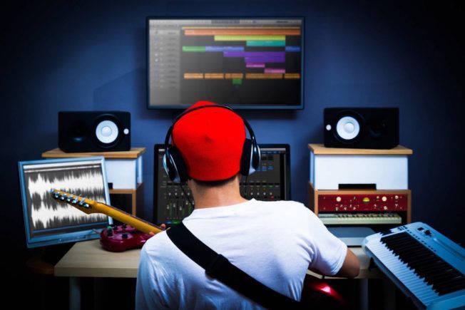 A man wearing headphones is playing a guitar in a recording studio.