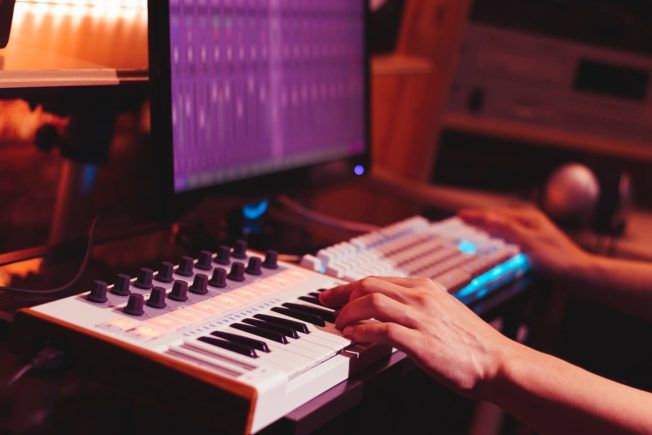 A person is playing a keyboard in front of a computer.