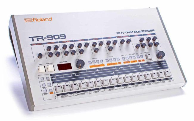 A roland tr-909 synthesizer is sitting on a white surface