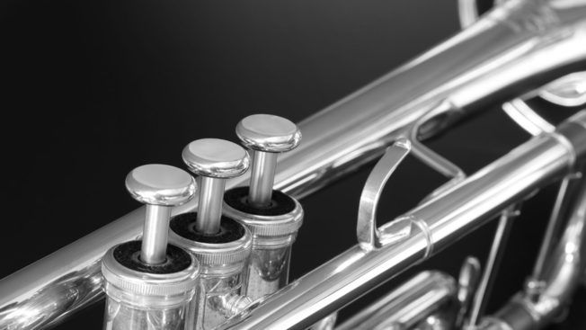 A close up of a silver trumpet on a black background.