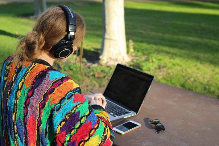 A woman wearing headphones is sitting at a table with a laptop and a cell phone.