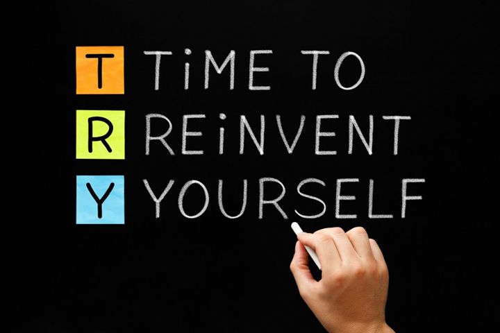 A person is writing on a blackboard that says time to reinvent yourself