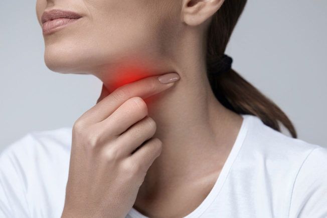 A woman is holding her throat with her hand because she has a sore throat.