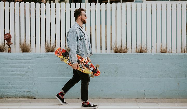 A man is walking down the street holding a skateboard.