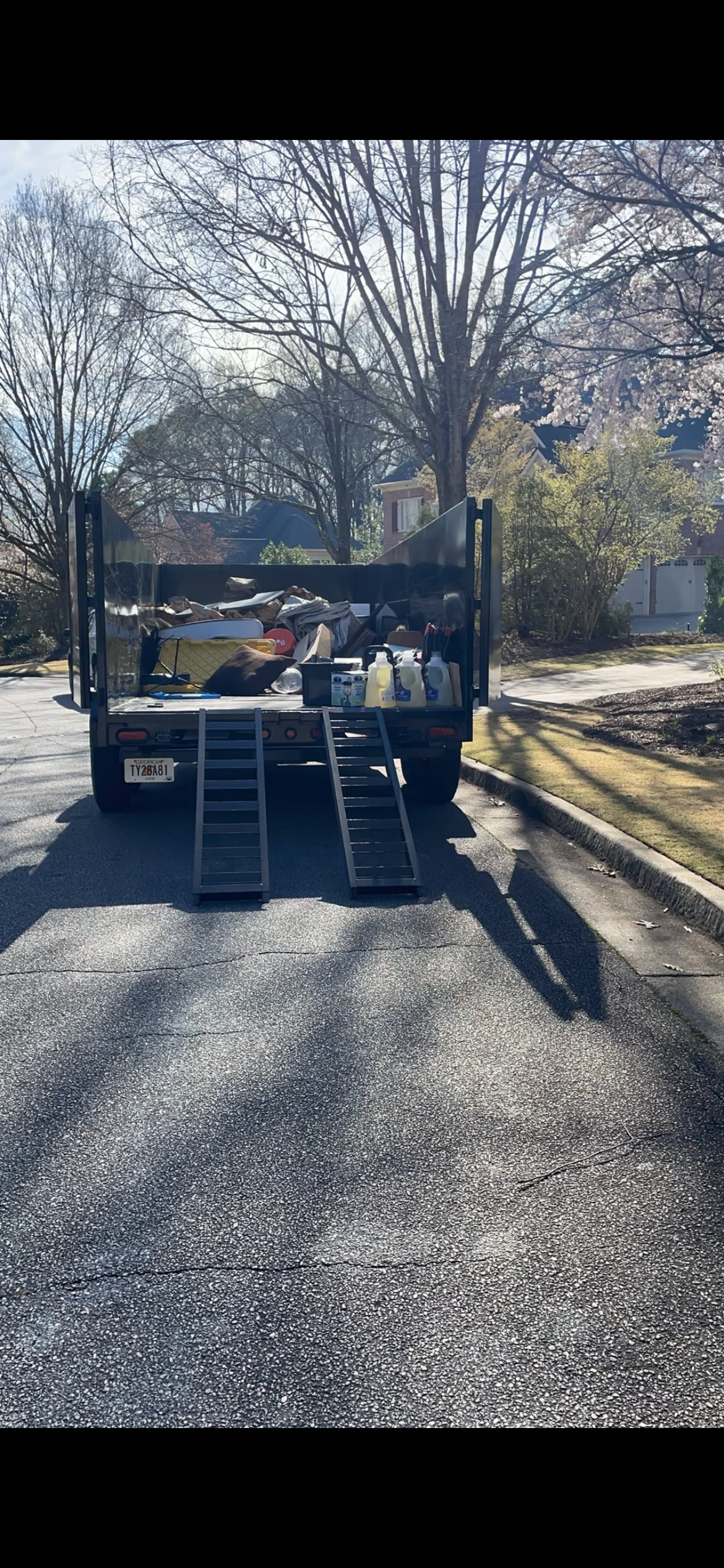 Truck unloading equipment down two ramps on a sunny residential street