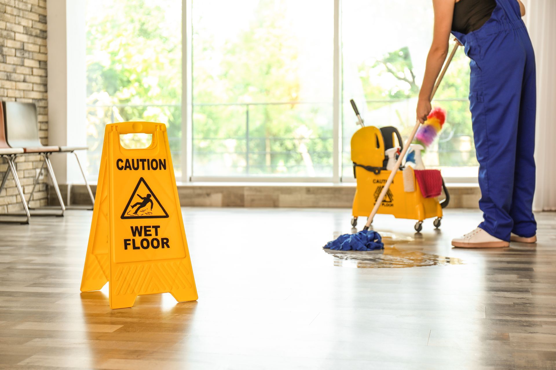 Caution wet floor sign beside a worker mopping a bright room floor