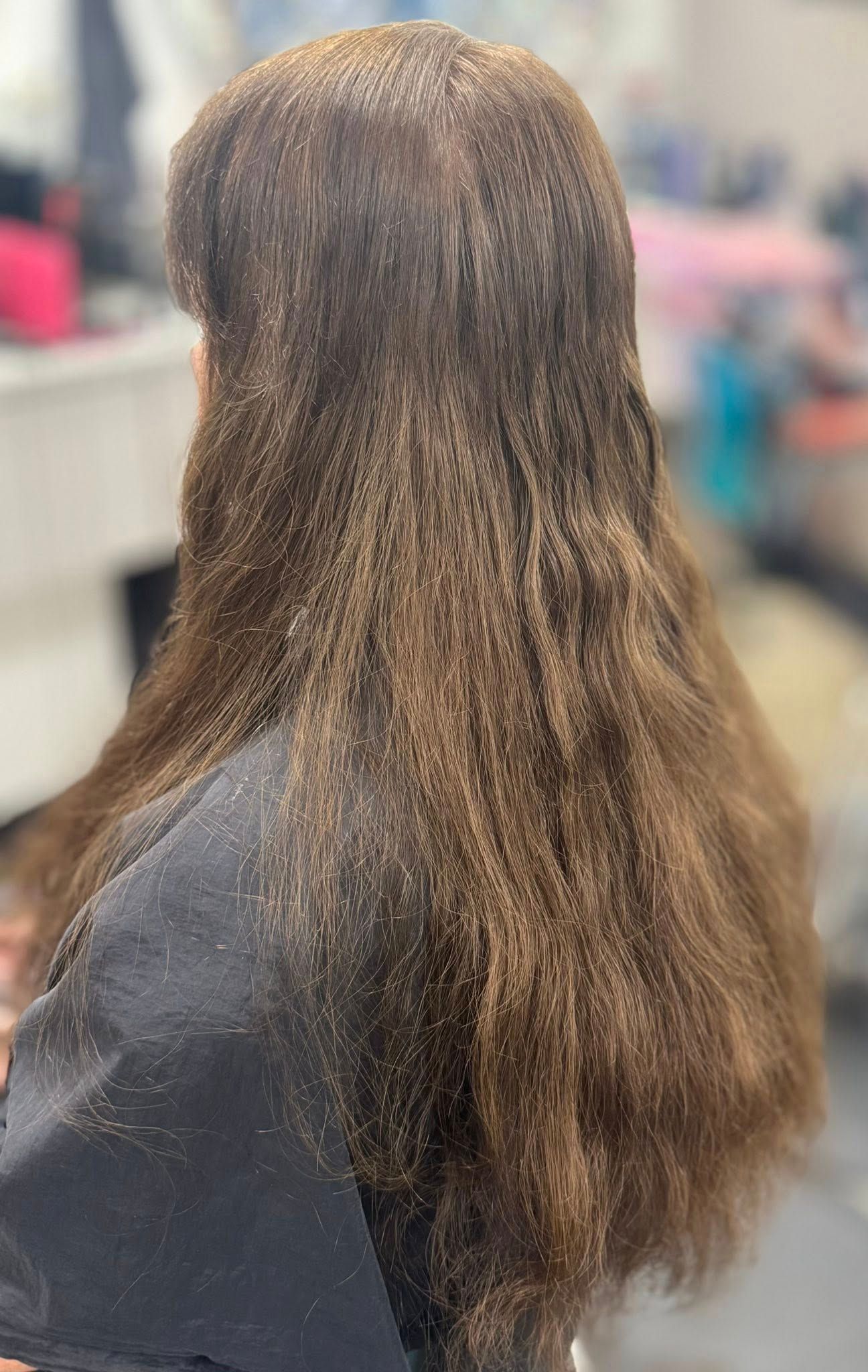 Back view of a person with long wavy brown hair in a salon chair