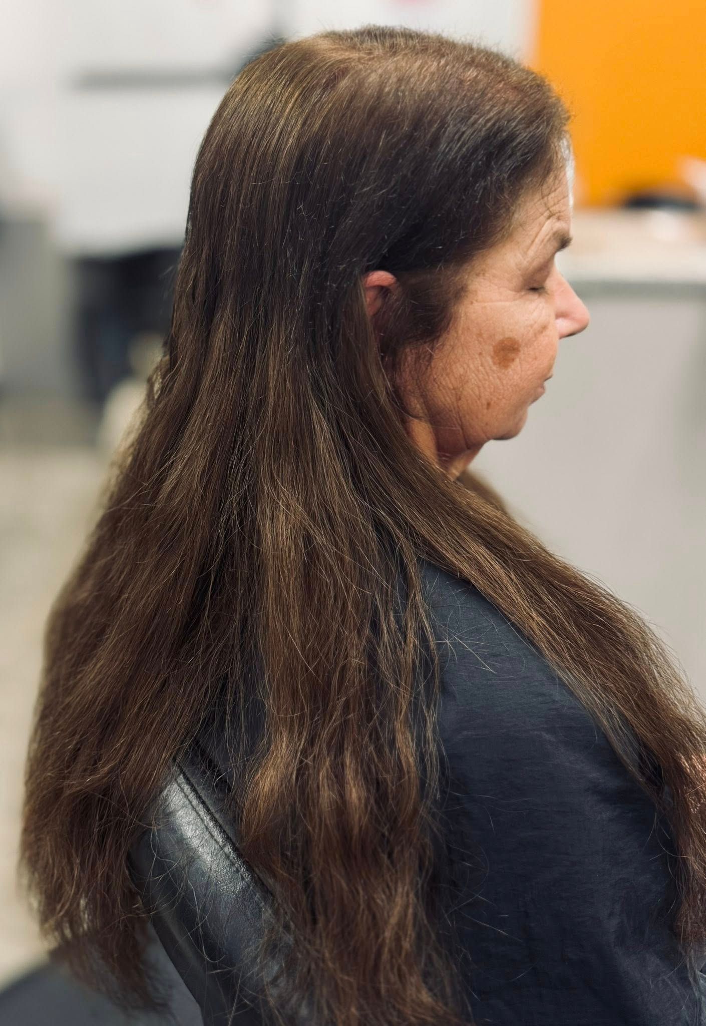 Side profile of a person with long brown hair seated indoors against a blurred office background.