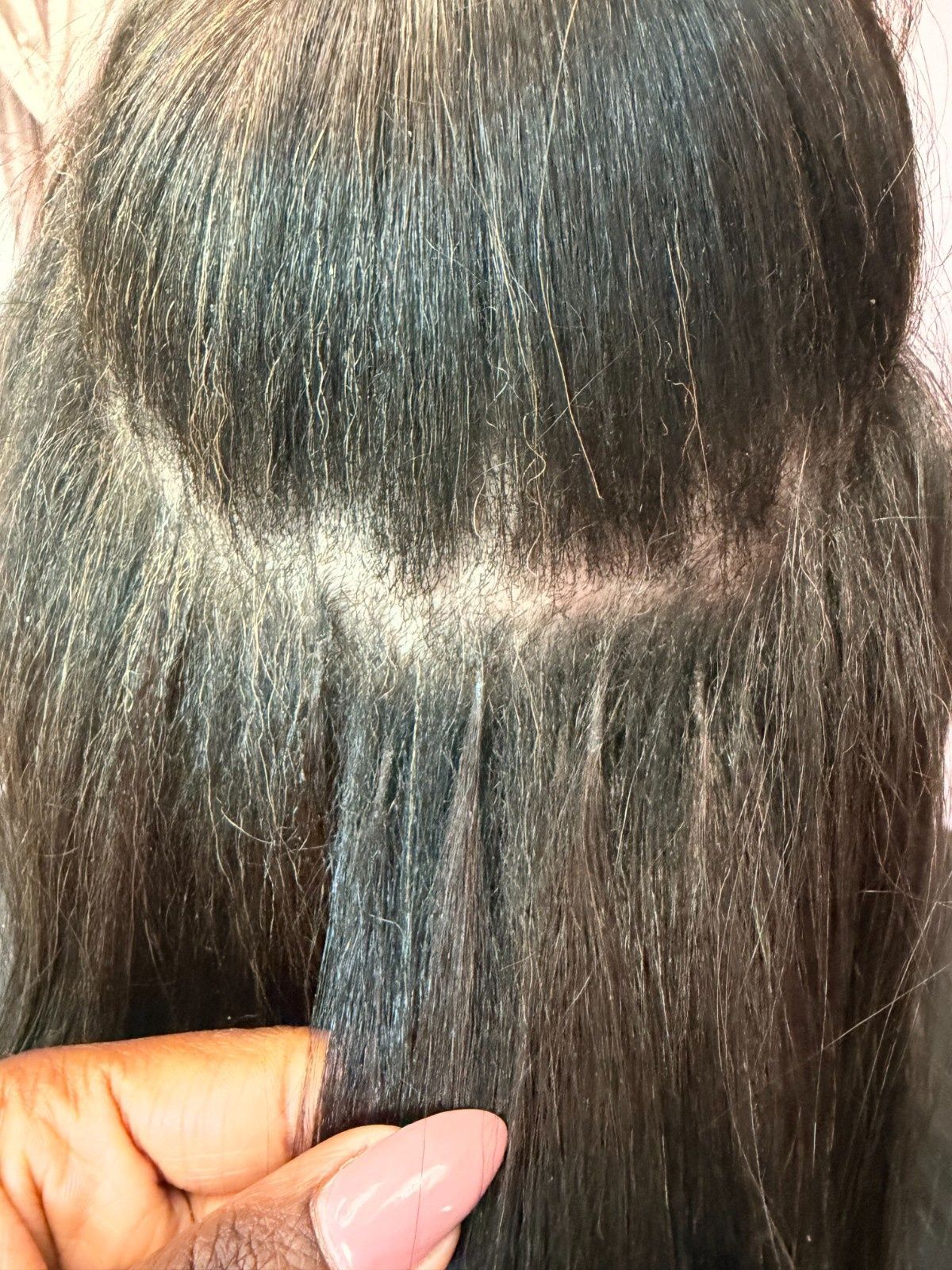 Close-up of dark hair with a visible scalp part, held between fingers.