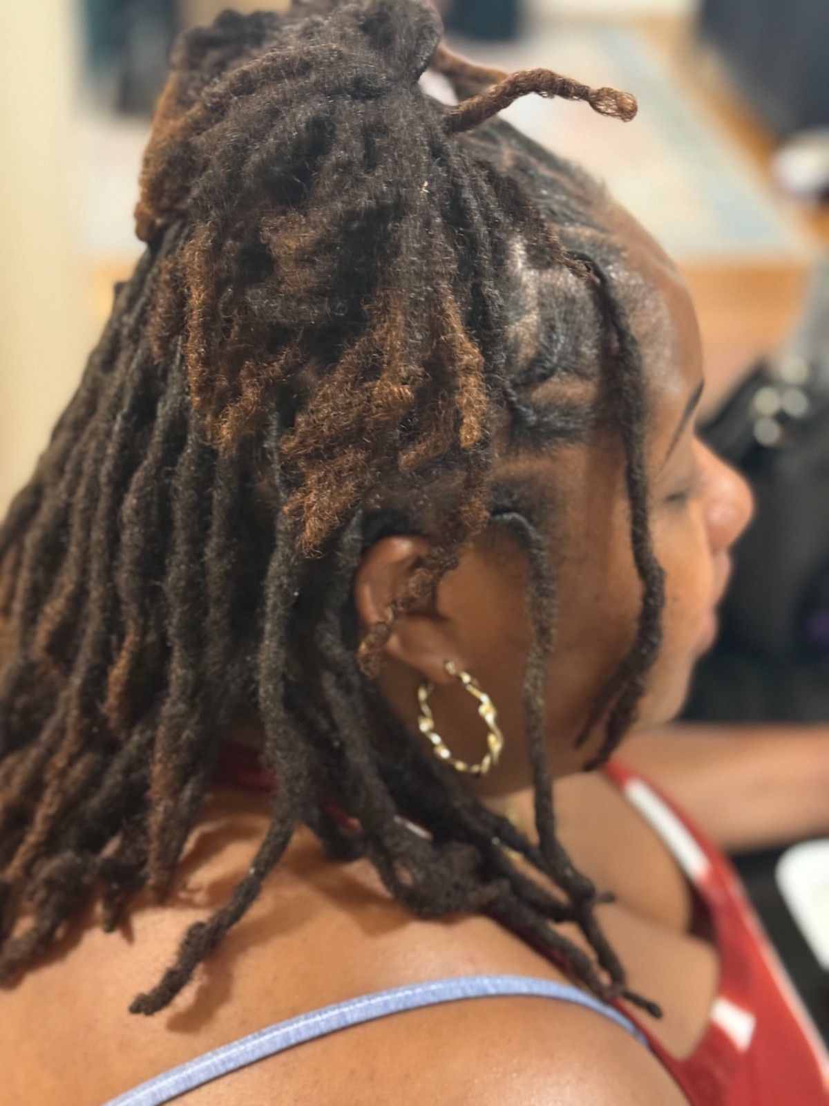 Side profile of a person with locs and hoop earrings, wearing a blue strap in a softly blurred indoor setting