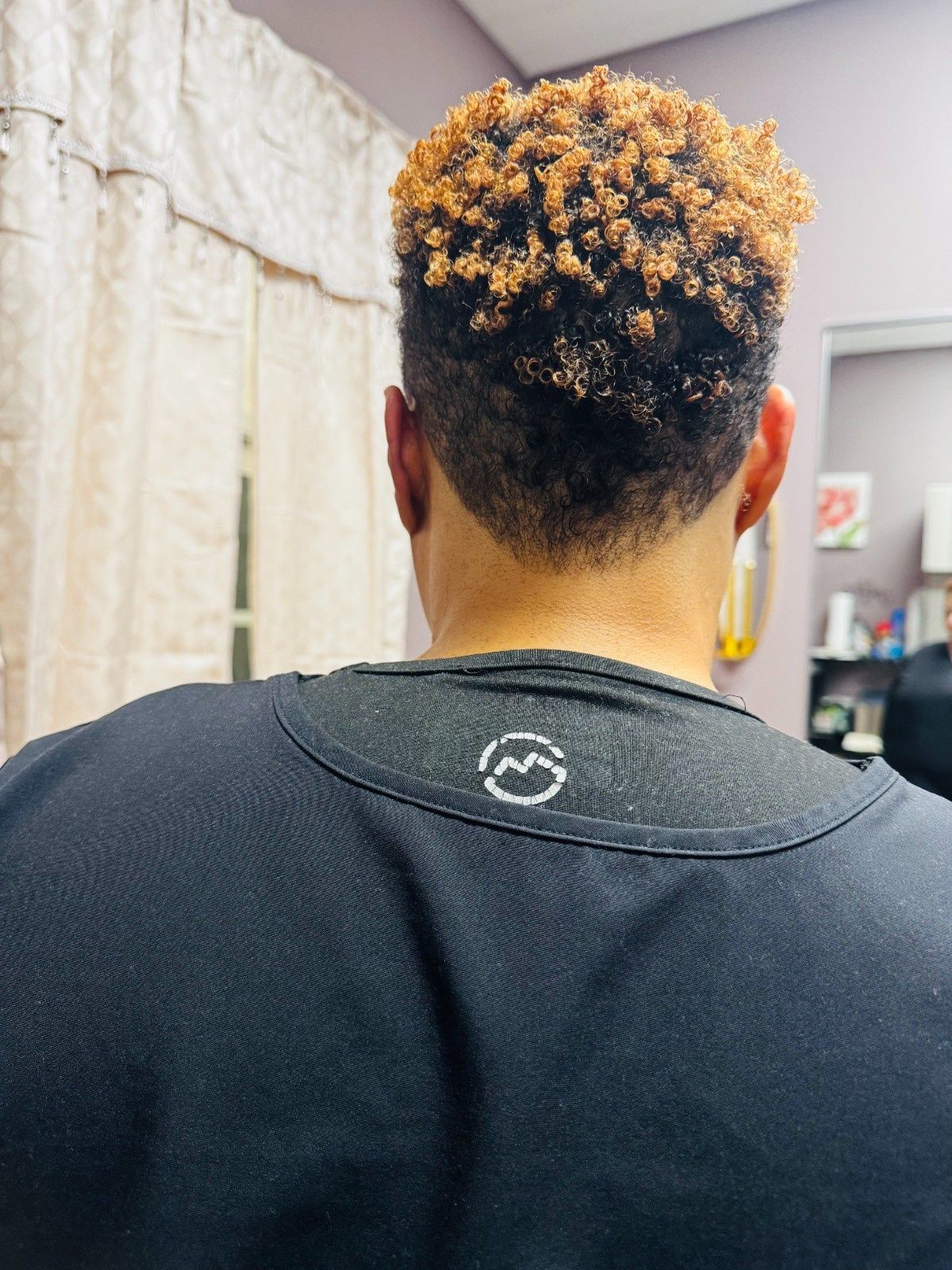 Back view of a person with short curly hair in a black shirt indoors
