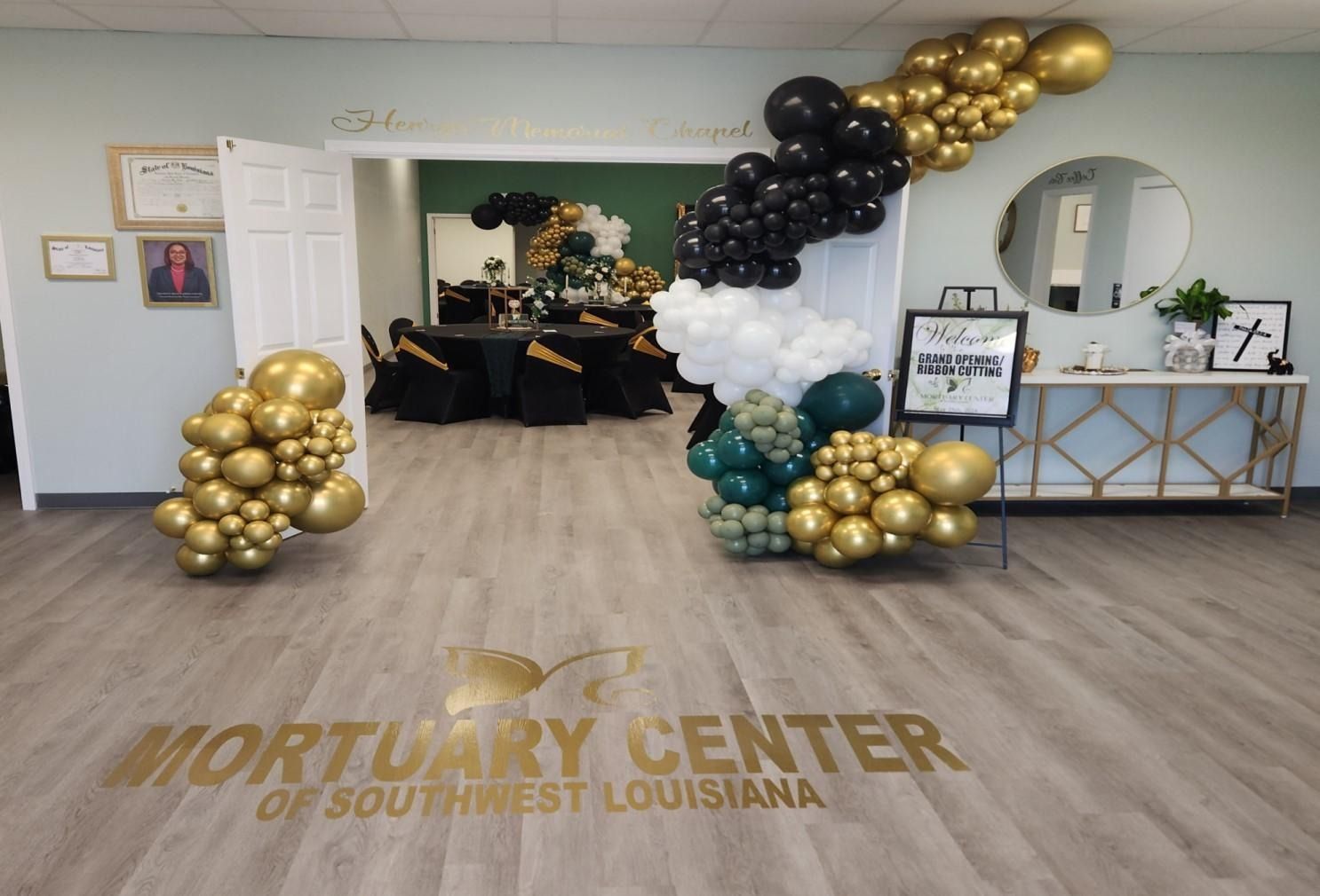 The Mortuary Center of Southwest Louisiana interior with gold, black, white, and green balloon arches and decor.