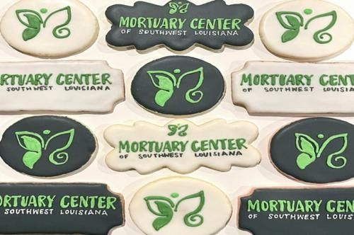 Cookies decorated with the Mortuary Center of Southwest Louisiana logo, featuring green butterfly motifs on dark backgrounds.