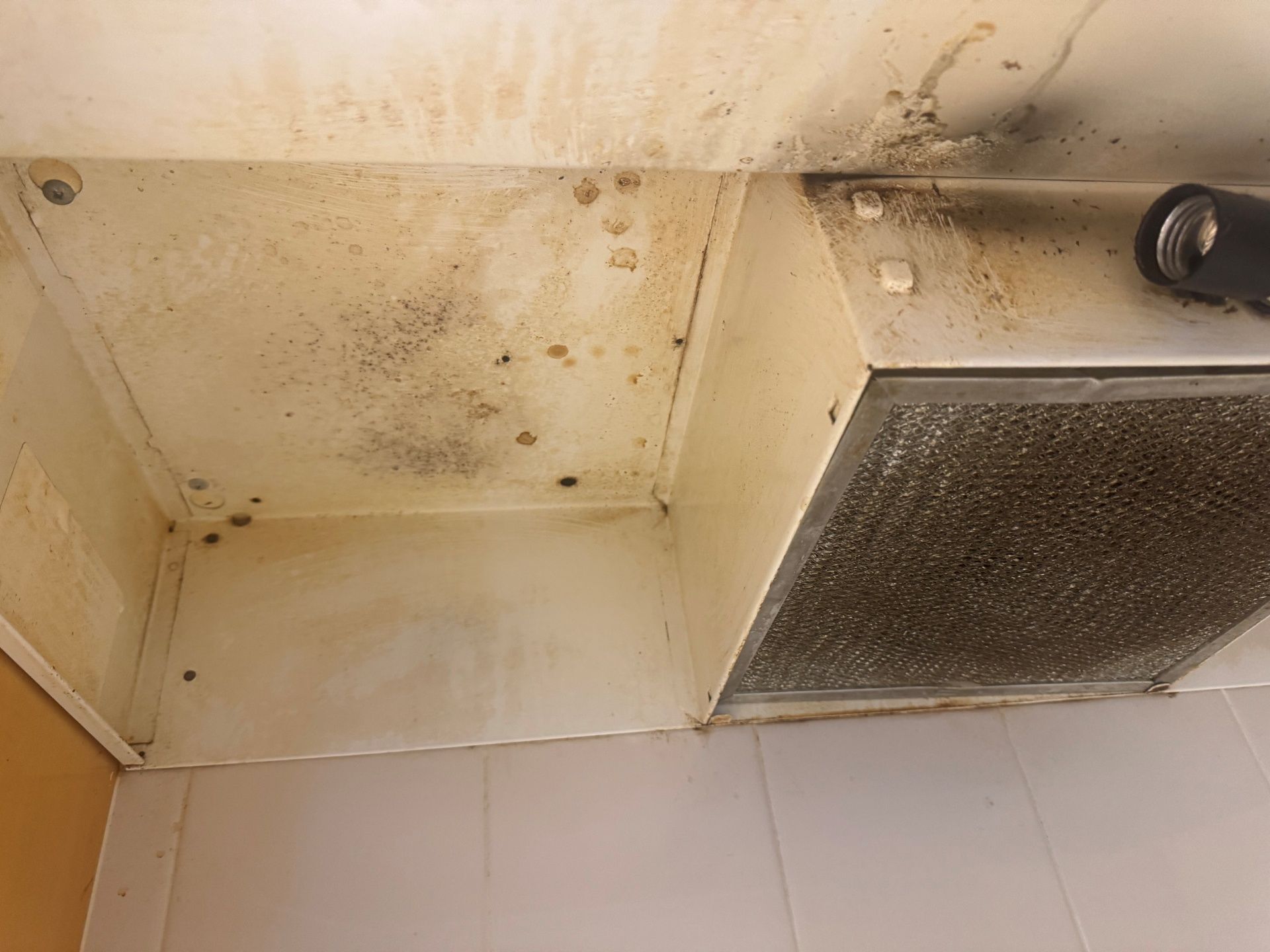 Dirty range hood, stained with grease and grime, above a tiled surface.