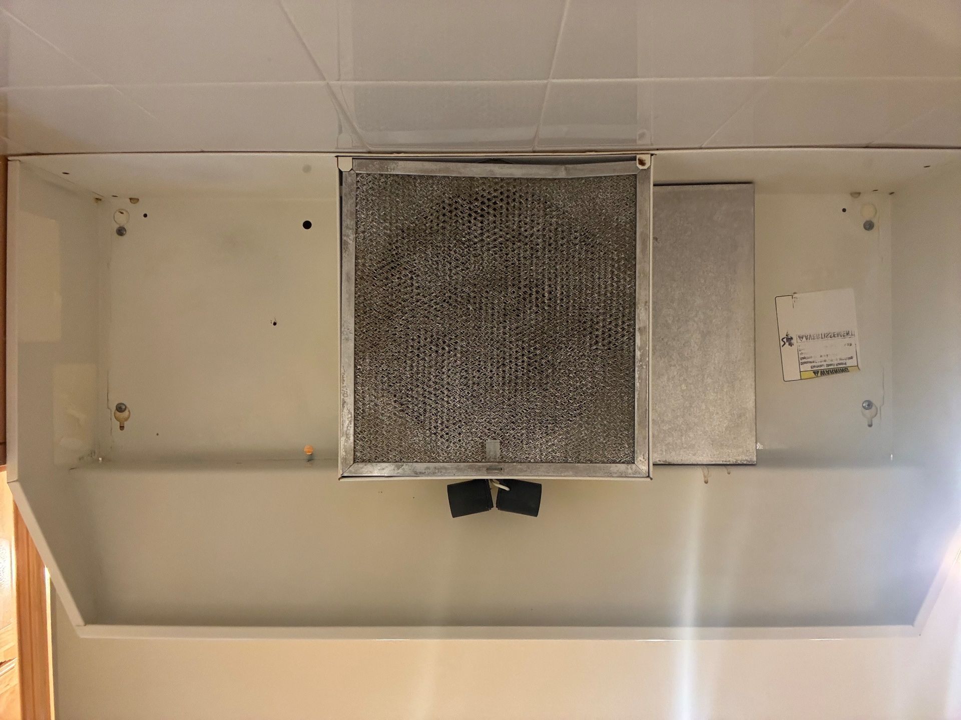 A dirty range hood filter in a white kitchen hood, likely needing cleaning or replacement.
