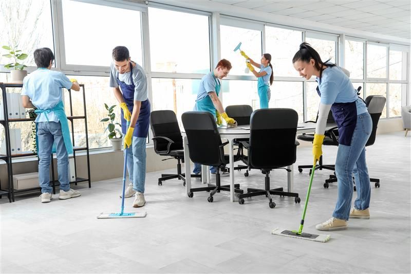 Office cleaners mopping the floor and wiping windows in a bright office.