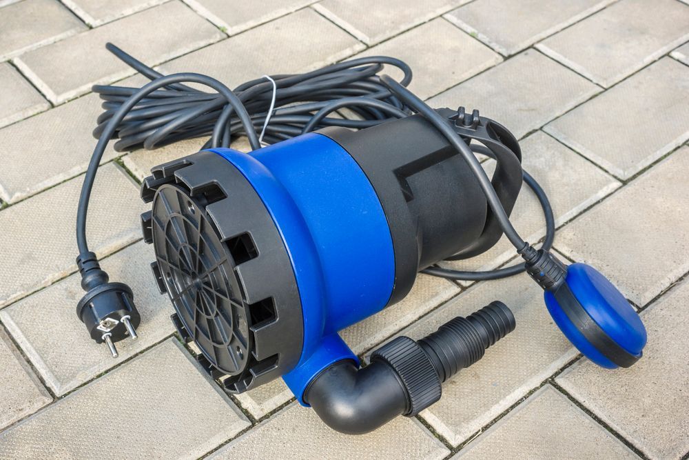 Bomba de agua sumergible azul y negra con interruptor de flotador, sobre adoquines de ladrillo.