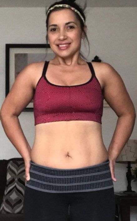 A woman in a red sports bra and black pants is standing in a living room.