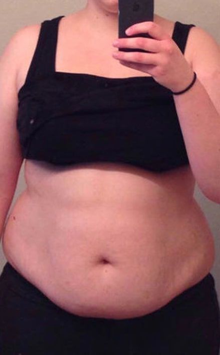 A woman is taking a selfie of her stomach with a cell phone.