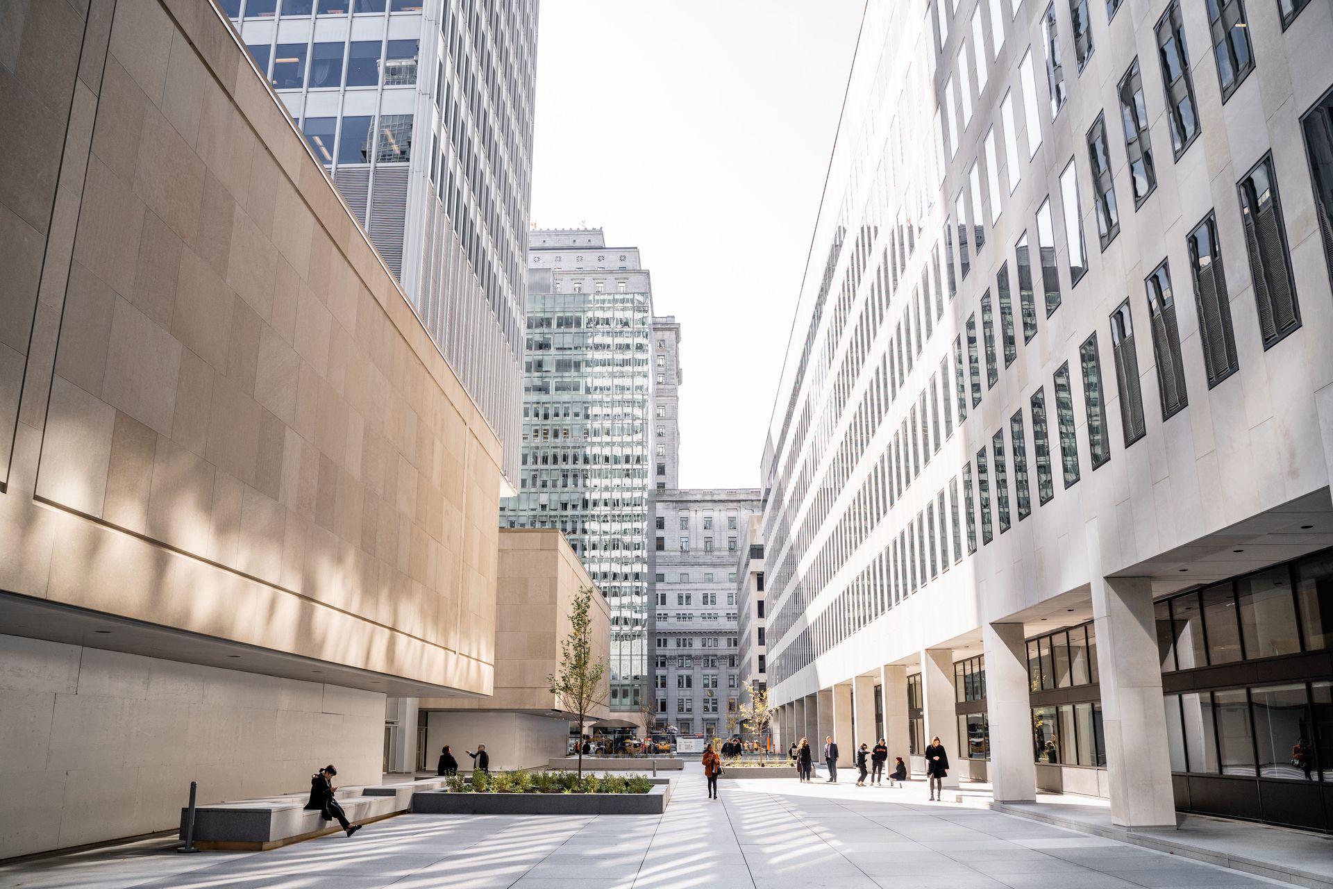 Exterior view of modern buildings with pedestrians on a plaza; natural light.
