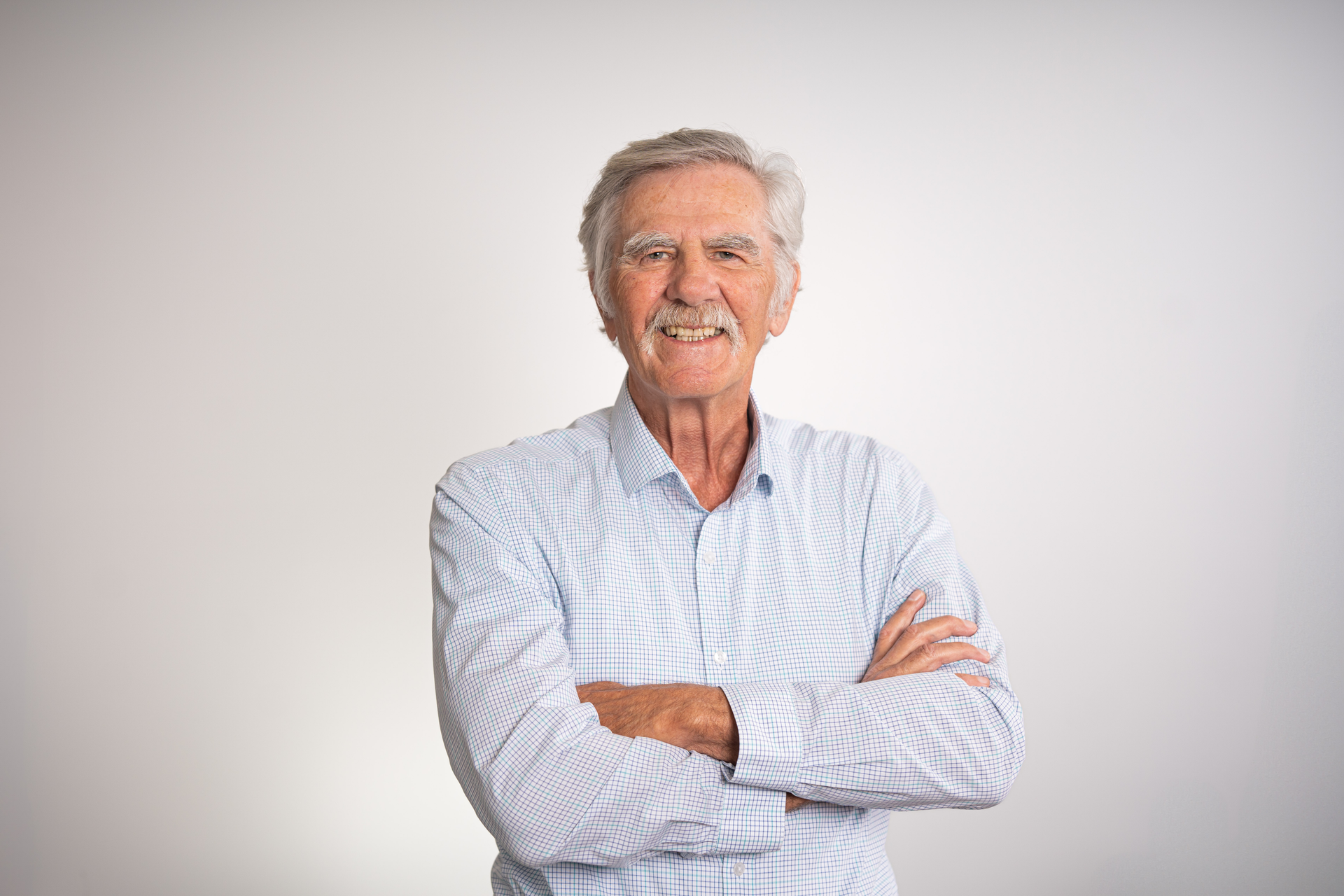Smiling man in dark suit and blue shirt against a white backdrop.