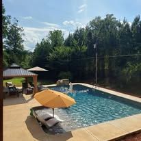 Swimming pool with umbrella, chairs, and trees on a sunny day.