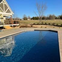 Outdoor swimming pool next to a house with a wooden deck; sunny day.