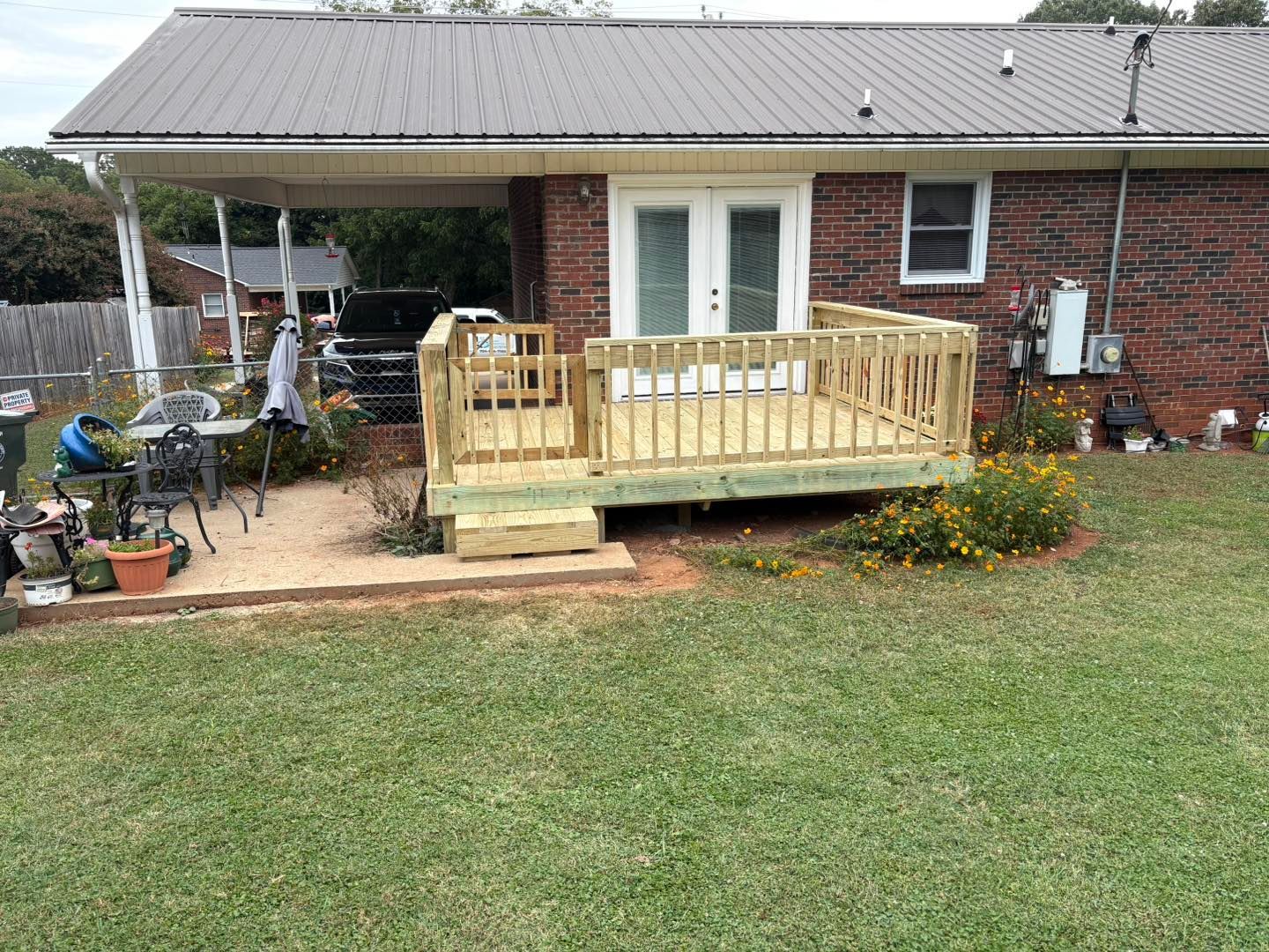 A newly built wooden deck with railing and steps in a backyard setting, next to a brick house.