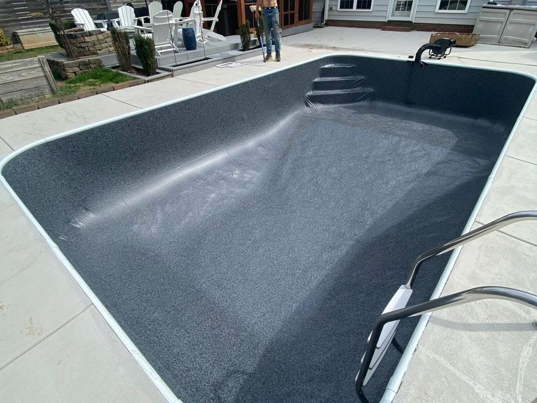 Empty, rectangular swimming pool with dark gray interior, steps, and handrails. Concrete surround.