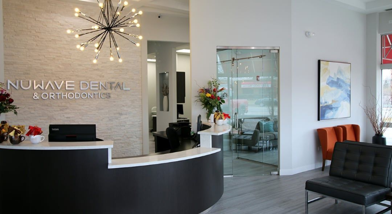 Modern dental office reception with black desk, starburst light, glass doors, and waiting chairs
