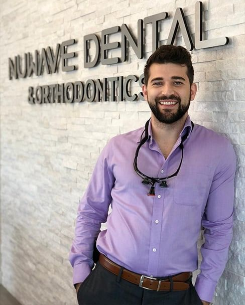 Smiling man in purple shirt standing in front of NuVive Dental Orthodontics sign