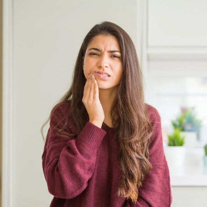 Woman holding her cheek with a pained expression in a bright kitchen