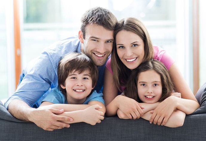 Smiling family of four leaning over a couch in a bright living room