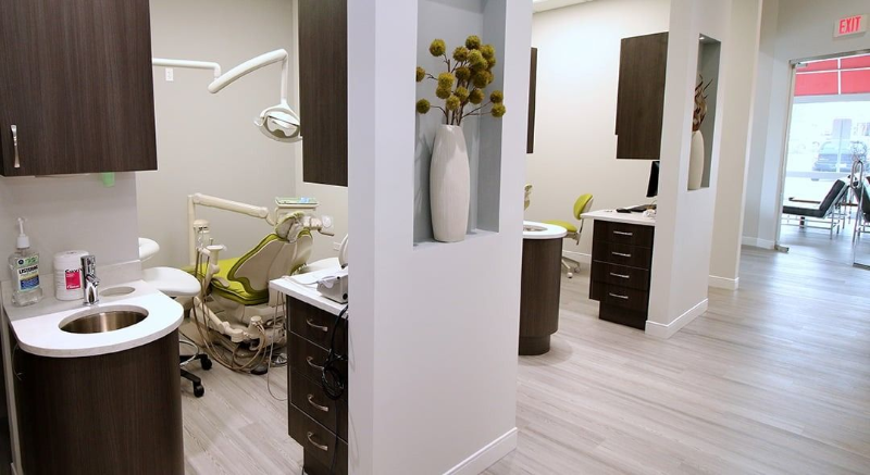 Modern dental office hallway with treatment room, chairs, sinks, and dark wood cabinets