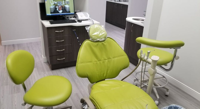 Dental exam room with green chairs, a monitor on the desk, and dental equipment in the foreground