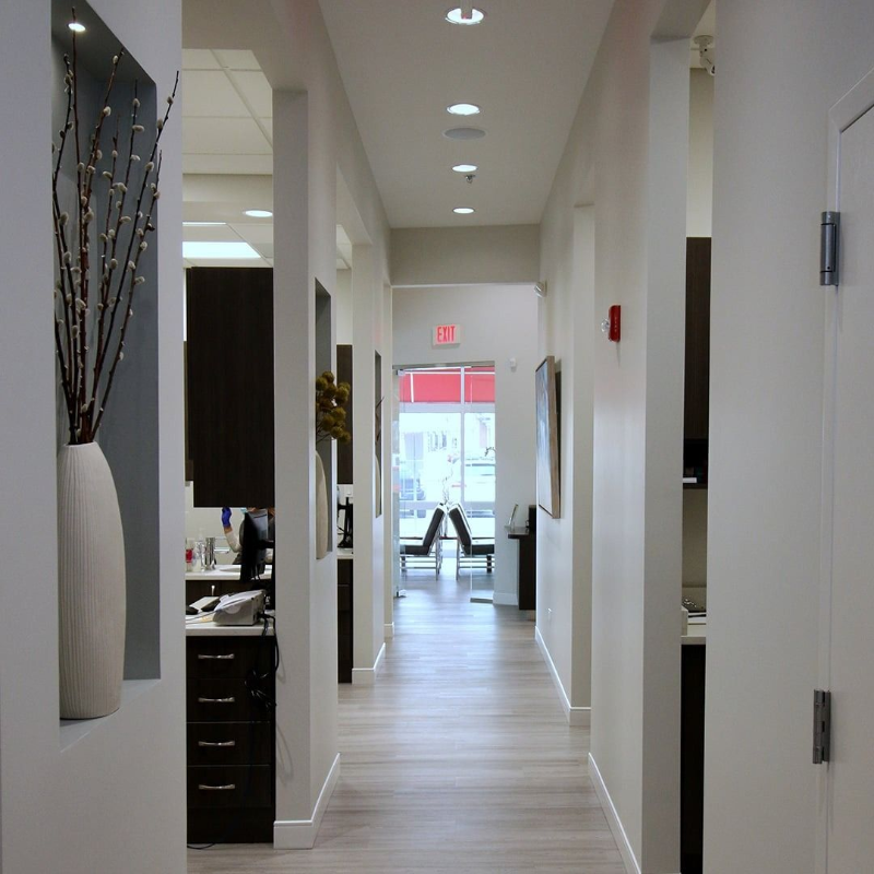 Bright office hallway with white walls, recessed lights, and an open glass doorway at the end