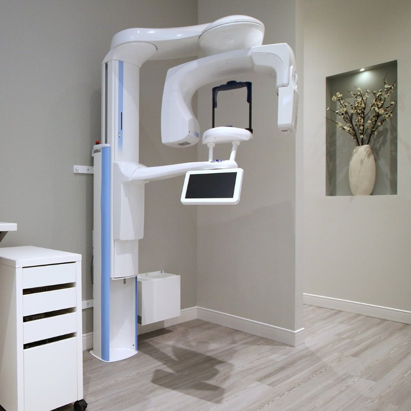 Dental X-ray machine in a modern exam room with a monitor and cabinet drawers