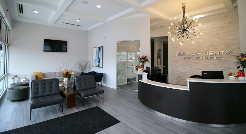 Modern dental office reception with curved black desk, waiting chairs, and chandelier lighting