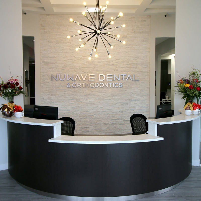 Modern dental office reception with curved black-and-white desk and chandelier under NuView Dental Orthodontics sign