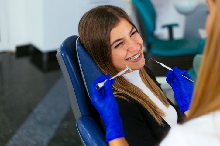 Woman smiling during dental treatment as a dentist examines her teeth with tools.