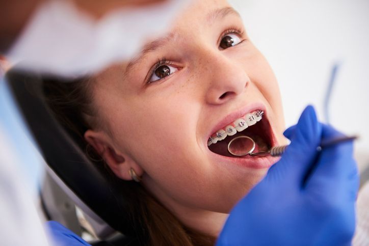 Child with braces having a dental checkup while wearing blue gloves and using a dental tool