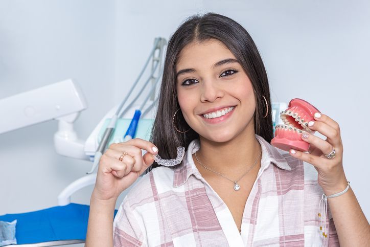 Smiling woman holding clear aligner and dental model in a bright dental clinic