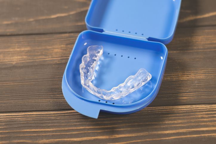 Clear dental aligner in an open blue case on a wooden surface