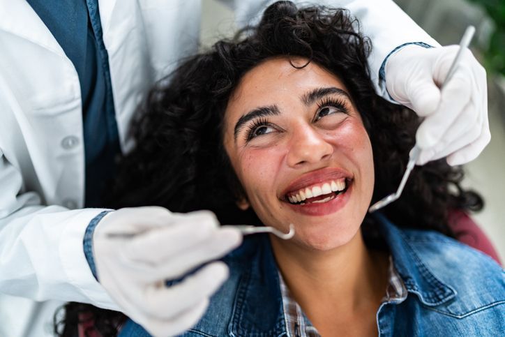 Dentist examining a smiling patient in a denim jacket with dental tools and gloves
